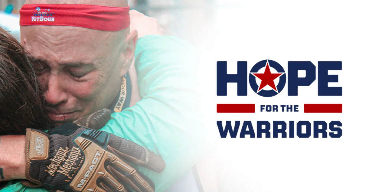 A veteran embraces a loved one beside the Hope for the Warriors logo